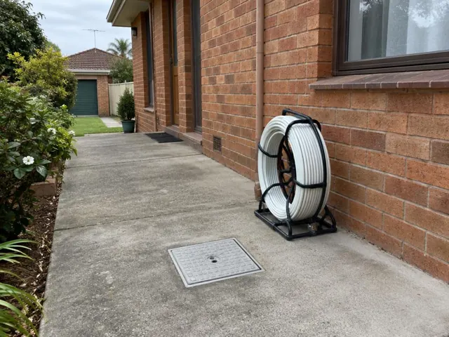 Concrete driveway beside a brick house with a flush capped access cover and tidy reinstated paving in Pagewood