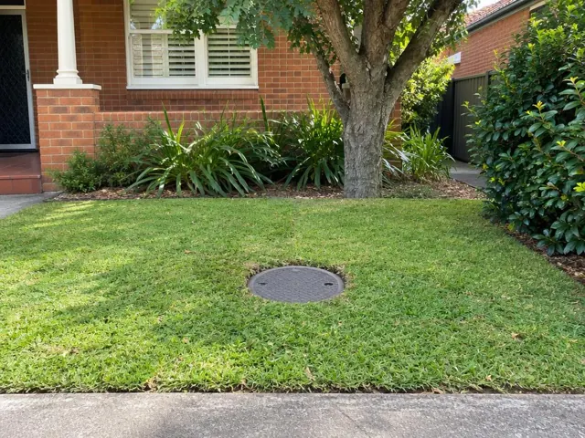 Lawn with a round capped sewer access cover near a brick house in Mascot